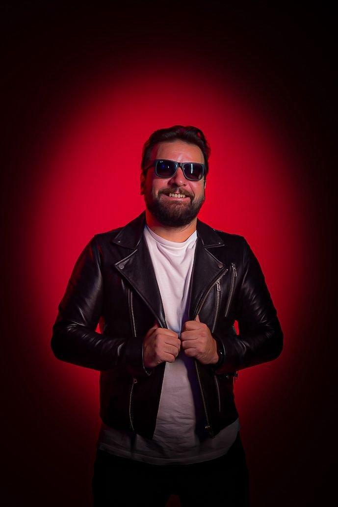 Retrato de Esteban Toledo sonriendo con anteojos oscuros sobre un fondo rojo